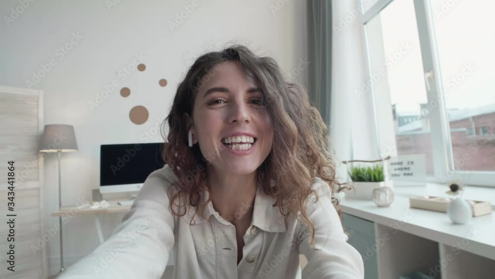 Medium shot portrait of Caucasian smiling woman with curly hair staying home and having video conversation with relatives Medium shot portrait of Caucasian smiling woman with curly hair staying home and having video conversation with relatives