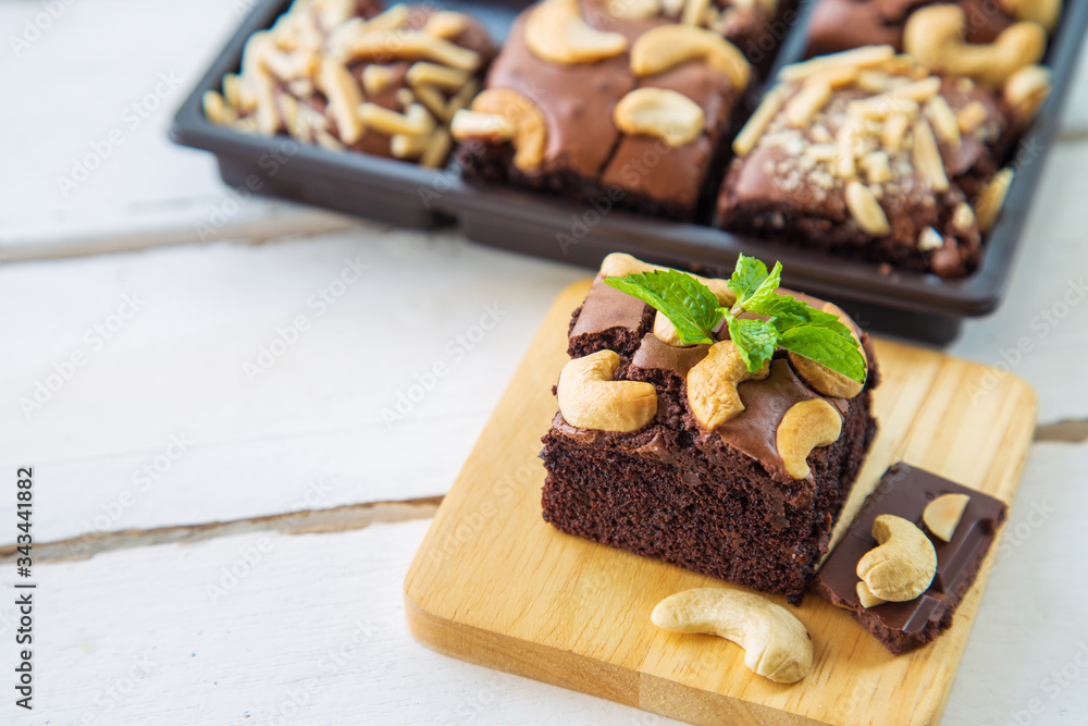 Chocolate brownies with cashew nut and papermint on wooden plate on white wooden floor with brownies box ackground.