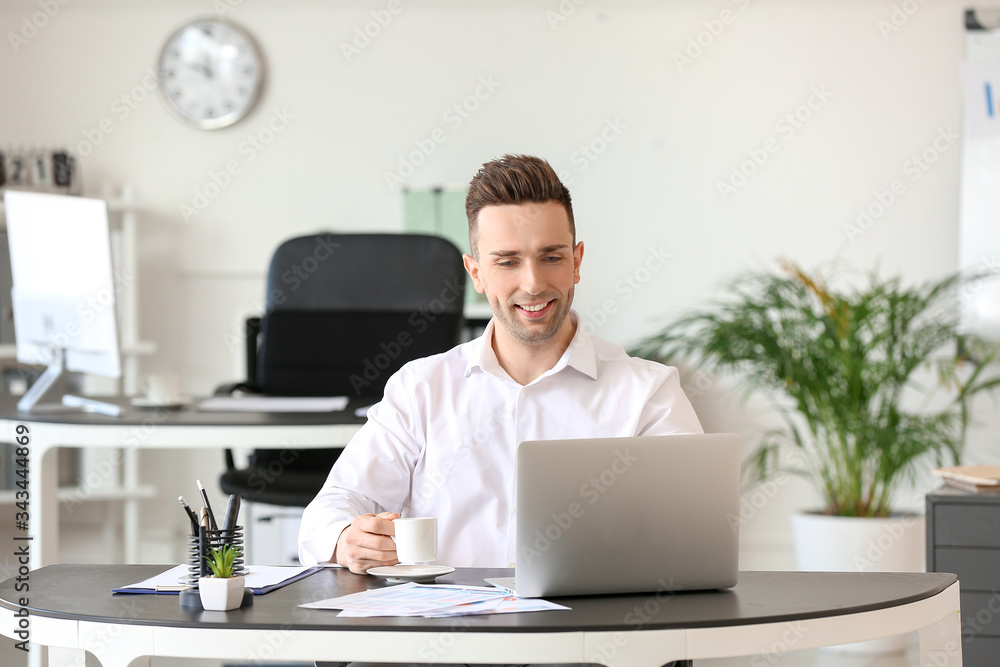 Man drinking coffee while working on laptop in office