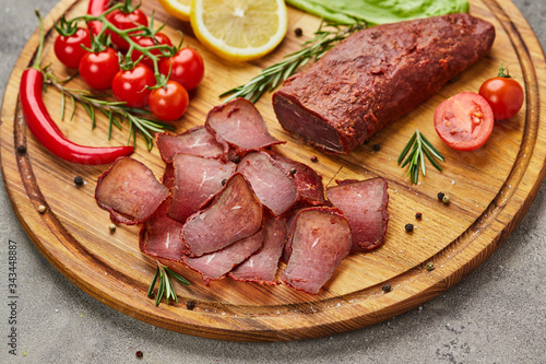 Armenian basturma or Pastirma on wooden cutting board decorated with spices, lettuce, lemon and tomatoes. Meat smoked jerky good as Beer snack