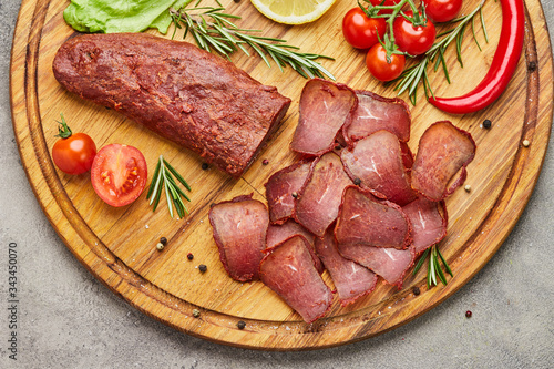 Armenian basturma or Pastirma on wooden cutting board decorated with spices, lettuce, lemon and tomatoes. Meat smoked jerky good as Beer snack