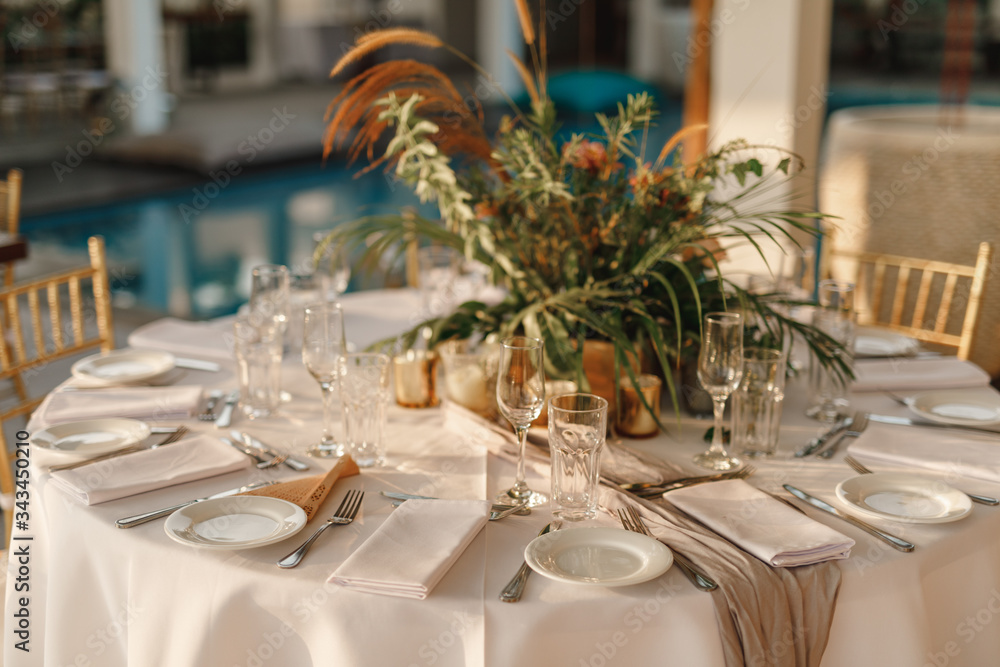 Wedding. Banquet. Round table for guests, served with cutlery, greenery flowers and crockery and covered with a white tablecloth Wedding. Banquet. Round table for guests, served with cutlery, greenery flowers and crockery and covered with a white tablecloth