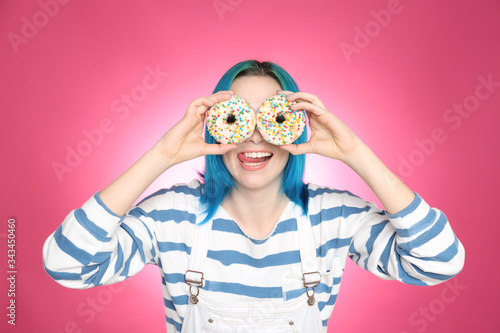 Young woman with bright dyed hair holding donuts on pink background