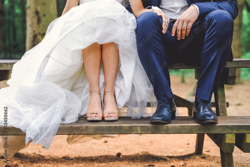 Foto Stock Ambiance Mariage champêtre. Mariés assis sur une table en bois.  Robe blanche, costume bleu, jambes, pieds et chaussures de mariage. | Adobe  Stock