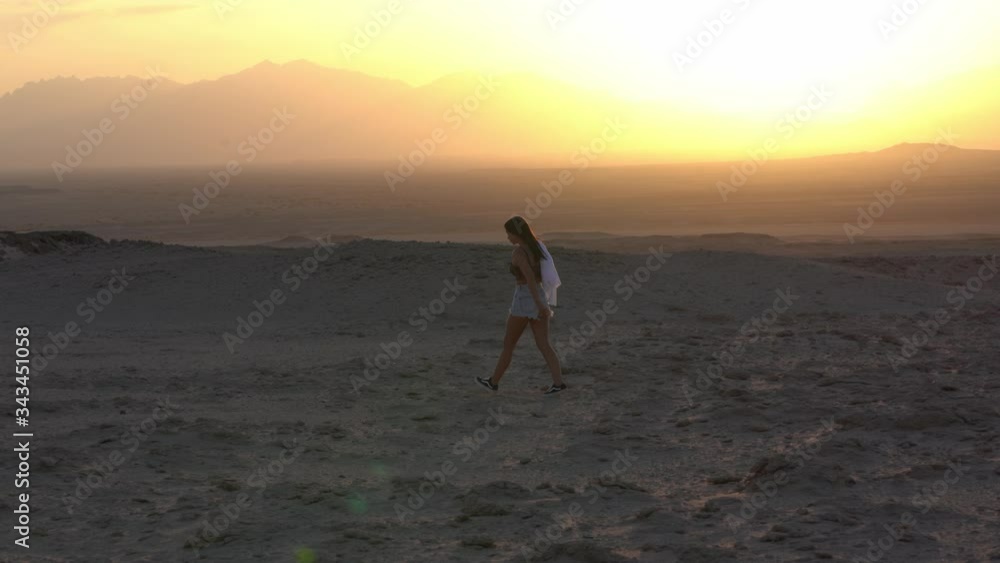 Beautiful Young Woman walking at Sunset in Sahara Desert with background of mountains and sun
Beautiful Young Woman walking at Sunset in Sahara Desert with background of mountains and sun