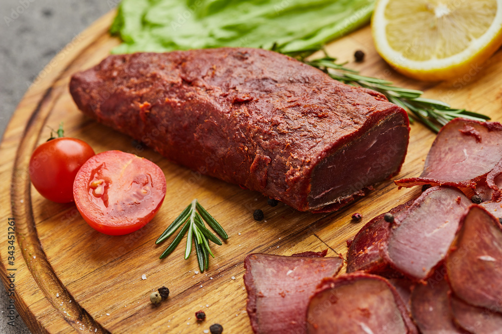 Armenian basturma or Pastirma on wooden cutting board decorated with spices, lettuce, lemon and tomatoes. Meat smoked jerky good as Beer snack Armenian basturma or Pastirma on wooden cutting board decorated with spices, lettuce, lemon and tomatoes. Meat smoked jerky good as Beer snack