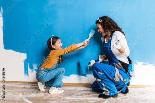 Mother and daughter enjoying together while painting wall. photo