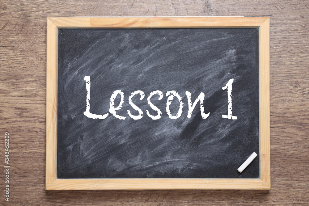 Fototapeta premium Blackboard with phrase LESSON 1 on wooden background, top view