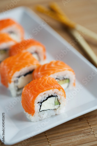 Delicious sushi roll with cheese, avocado and salmon on a white plate.