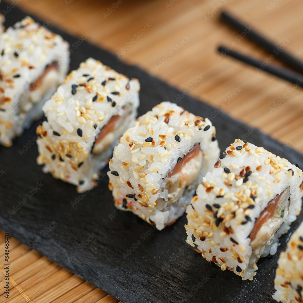 Uramaki served on a black slate with wooden black sticks and soy sauce. Japanese traditional food with bamboo service. Uramaki served on a black slate with wooden black sticks and soy sauce. Japanese traditional food with bamboo service.
