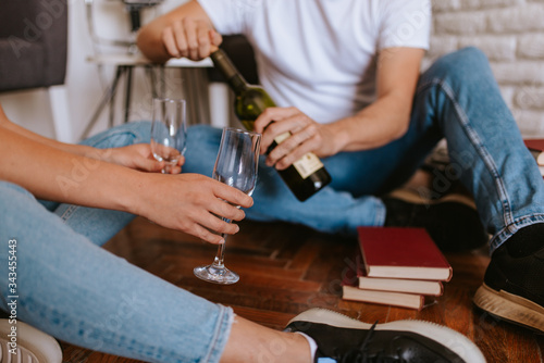 An attractive caucasian man and woman are sitting on the floor of a new apartment, drinking wine and celebrating. A loving couple moves in