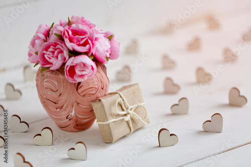 Decorative wooden hearts, vase with flowers and gift box on white textured wooden table.