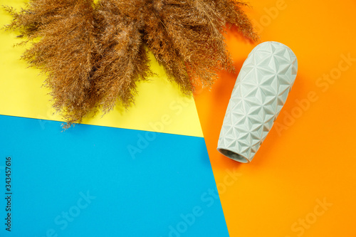 A minimalistic composition of a light turquoise ceramic vase, lies an empty vase on a colored background. Nearby are the branches of dry clumps. photo