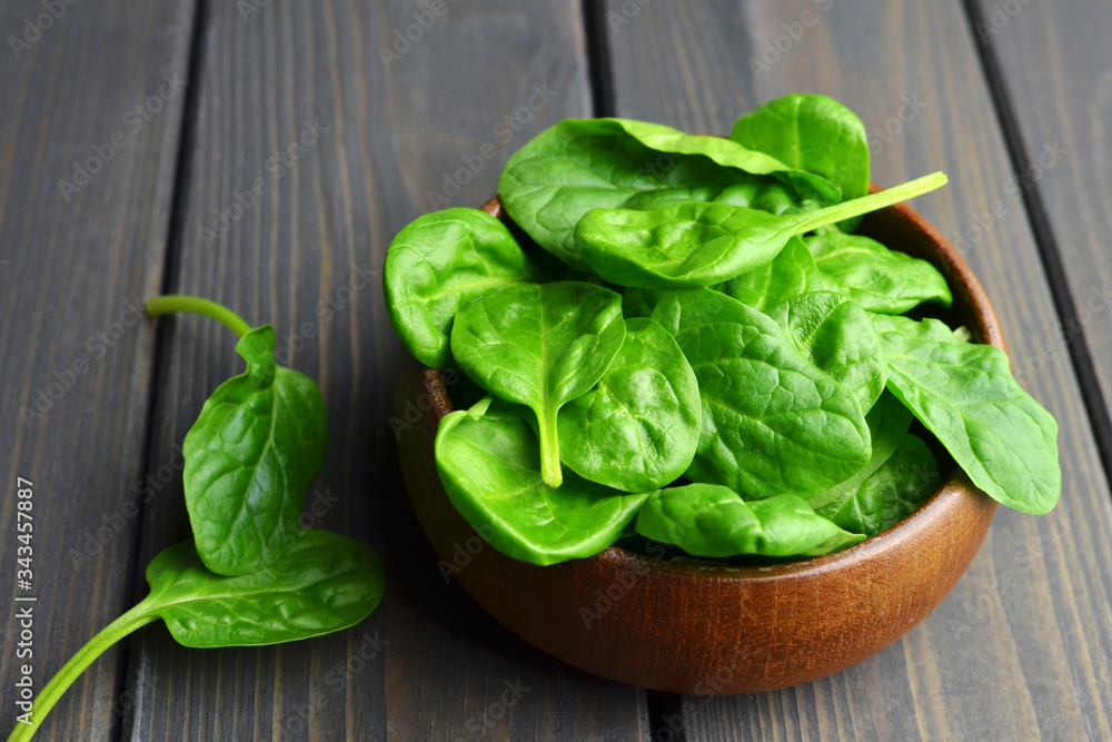 Fresh spinach leaves in wooden bowl over old wooden table. Healthy vegan food. Green living and eco-conscious concept. Fresh spinach leaves in wooden bowl over old wooden table. Healthy vegan food. Green living and eco-conscious concept.
