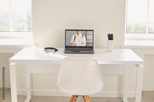 Doctor online. A stethoscope is on a white table with a laptop in blur at the hospital office.