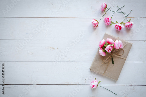 Gift box wrapped in kraft paper and pink vintage roses on white wooden background. Top view. Flat lay.