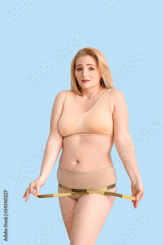 Sad overweight woman with measuring tape on color background. Weight loss concept