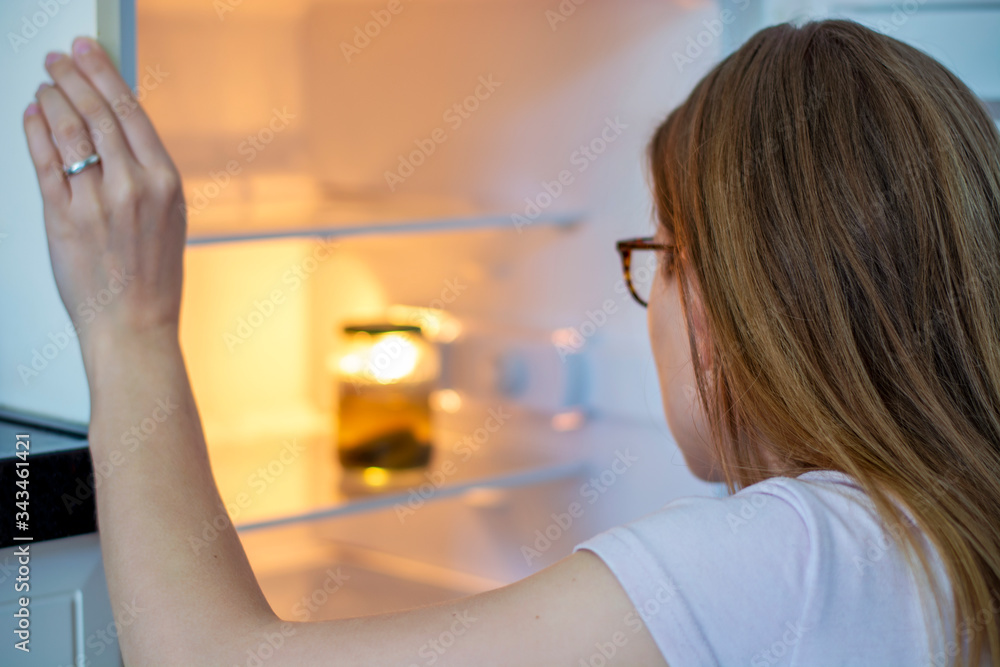Woman peers into a refrigerator and only sees a jar of pickles in