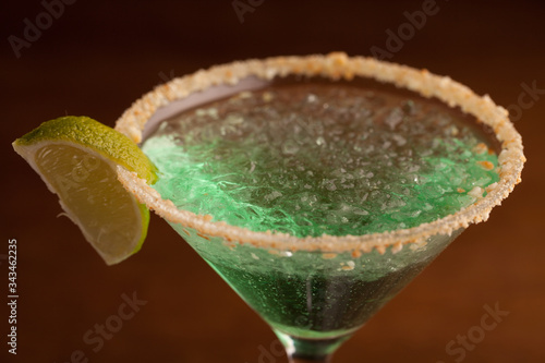 green cocktail in a martini glass rim covered with salt. with a slice of lime. close-up on a brown background