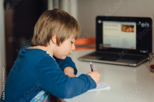 Kid studying online writing in his notebook. Studying home