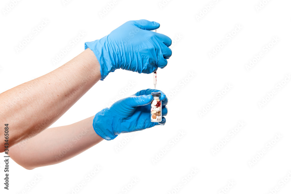 hands in blue medical gloves are holding a glass bottle with a vaccine different pills a drug into an injection syringe, medical theme close up isolated on white background with copy space. hands in blue medical gloves are holding a glass bottle with a vaccine different pills a drug into an injection syringe, medical theme close up isolated on white background with copy space.