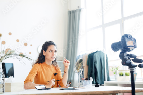 Beauty blogger sitting alone in her room explaining something to viewers, horizontal shot photo