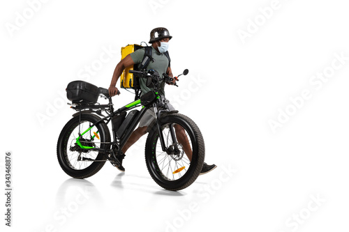 Too much orders. Contacless delivery service during quarantine. Man delivers food during isolation, wearing helmet and face mask. Taking food on bike isolated on white background. Safety. Hurrying up.