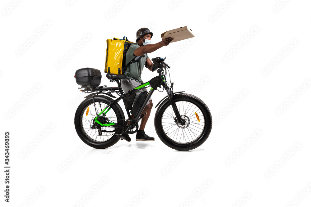Too much orders. Contacless delivery service during quarantine. Man delivers food during isolation, wearing helmet and face mask. Taking food on bike isolated on white background. Safety. Hurrying up. Too much orders. Contacless delivery service during quarantine. Man delivers food during isolation, wearing helmet and face mask. Taking food on bike isolated on white background. Safety. Hurrying up.
