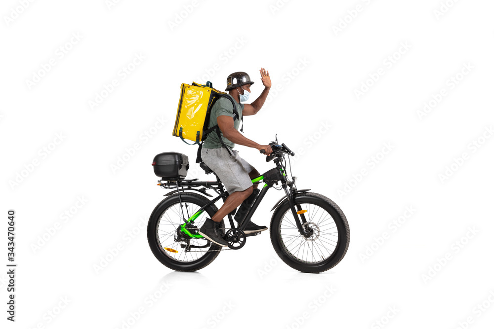 Too much orders. Contacless delivery service during quarantine. Man delivers food during isolation, wearing helmet and face mask. Taking food on bike isolated on white background. Safety. Hurrying up. Too much orders. Contacless delivery service during quarantine. Man delivers food during isolation, wearing helmet and face mask. Taking food on bike isolated on white background. Safety. Hurrying up.
