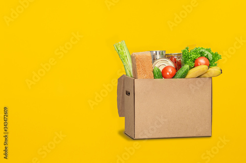 Donation box with food on a yellow background. Coronavirus food delivery. Volunteer brings a box of food. Donation, quarantine concept. Volunteer collecting food. Copyspace.