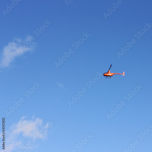 Private small orange helicopter on a background of blue sky