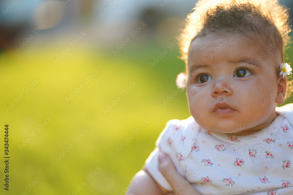 Beautiful baby portrait looking up to the sky during sunset wearing 4 months to 6 month baby suit. Green grass backgrounds and sun that comes from the back of the baby. 85mm lens photography Beautiful baby portrait looking up to the sky during sunset wearing 4 months to 6 month baby suit. Green grass backgrounds and sun that comes from the back of the baby. 85mm lens photography