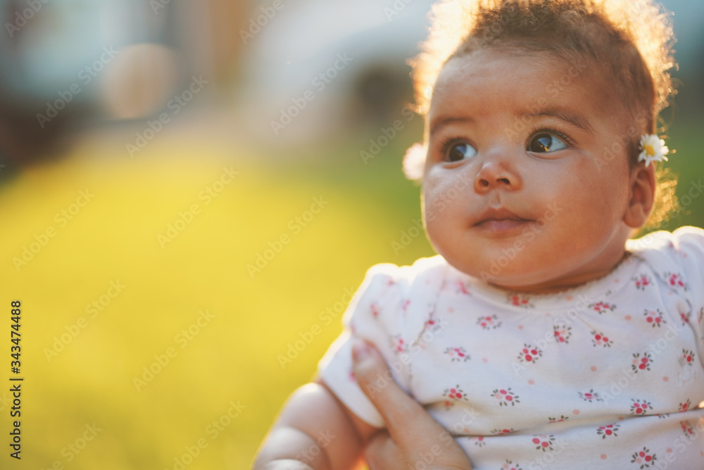 Beautiful baby portrait looking up to the sky during sunset wearing 4 months to 6 month baby suit. Green grass backgrounds and sun that comes from the back of the baby. 85mm lens photography