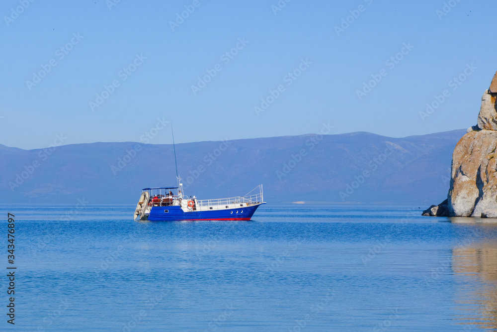 A pleasure tourist boat floats on the water of Lake Baikal. Rocky cape Burhan near the island of Olkhon, Russia.