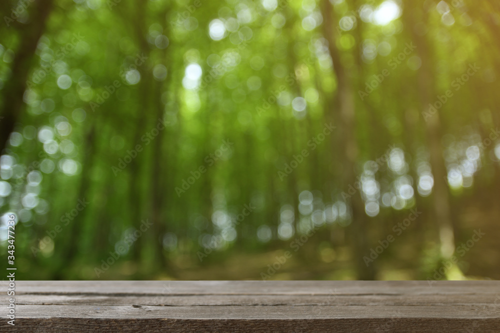 Image of grey wooden table in front of abstract blurred background of green leaves and trees Image of grey wooden table in front of abstract blurred background of green leaves and trees