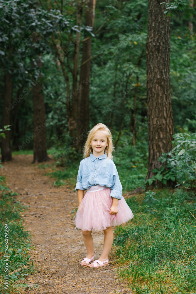 A small blonde girl of five in romantic clothes walks along a forest path and smiles A small blonde girl of five in romantic clothes walks along a forest path and smiles