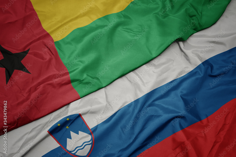 waving colorful flag of slovenia and national flag of guinea bissau.