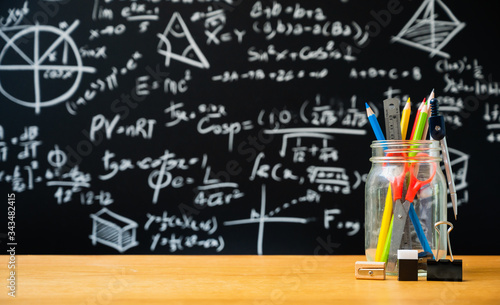 Education background concept. Stationery in glass jar color pencil, compasses tool, scissors, rulers, sharpener On chalkboard with the Mathematical formula background.