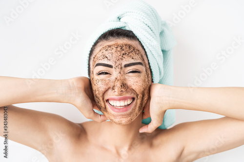 Foto Young smiling woman applying coffee scrub mask on face - Happy girl having skin