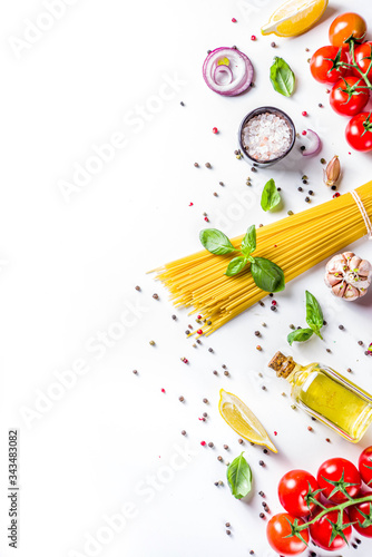 Italian food ingredients for cooking Spaghetti Pasta. Raw spaghetti pasta with various ingredient - onion, tomatoes, garlic, basil, parsley, cheese, olive oil. On white table background, flatlay copy