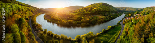 Panoramic aerial landscape shot of Neckar river  Germany  at a beautiful sunset  with clear sky and the vegetation being colorfully lit  a road following alongside the water