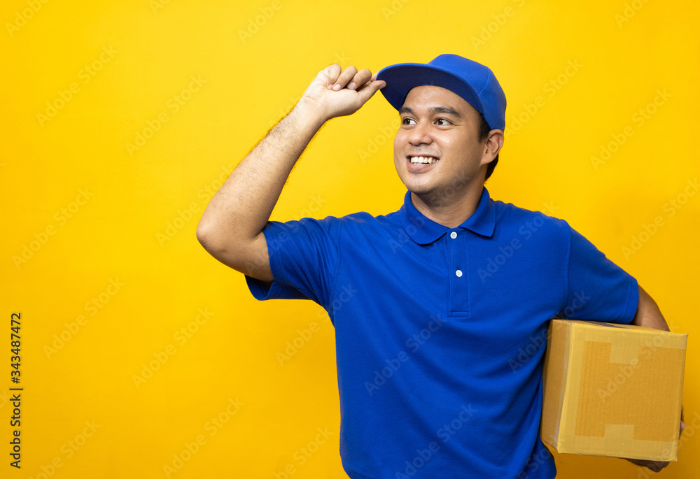 Blue Delivery handsome asian man holding parcel cardboard box on isolated yellow background. Blue Delivery handsome asian man holding parcel cardboard box on isolated yellow background.