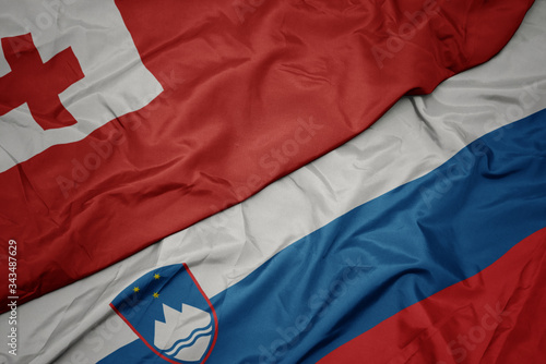 waving colorful flag of slovenia and national flag of Tonga .