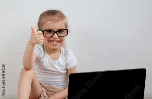 A child with glasses sits at a computer and shows a like.