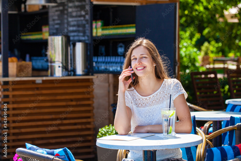 Happy brunette woman calling by phone in open air cafe