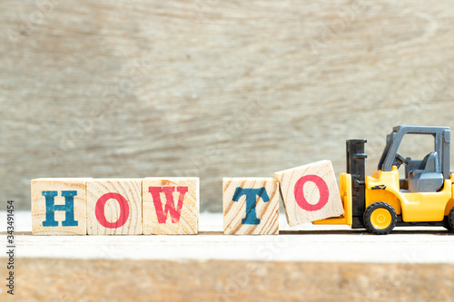 Billede på lærred Toy forklift hold letter block w to complete word how to on wood background
