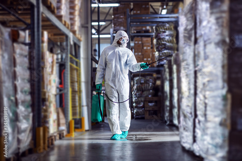 Man in protective suit and mask disinfecting warehouse full of food products from corona virus / covid-19. © dusanpetkovic1