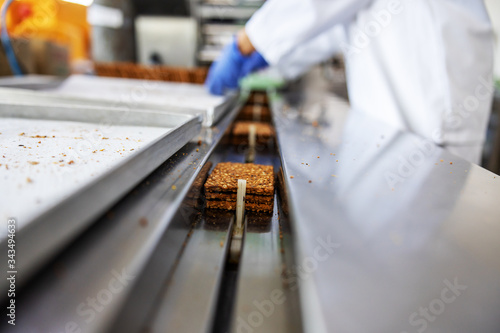 Closeup of worker picking up biscuits form machine while standing in food factory.
