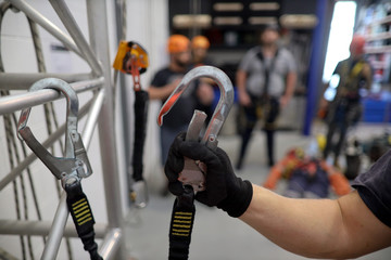 Trained competent instructor wearing a back hand safety glove clipping hook onto  round structure steel which its connecting into lanyard shock absorber selt retracting device as fall arrest system