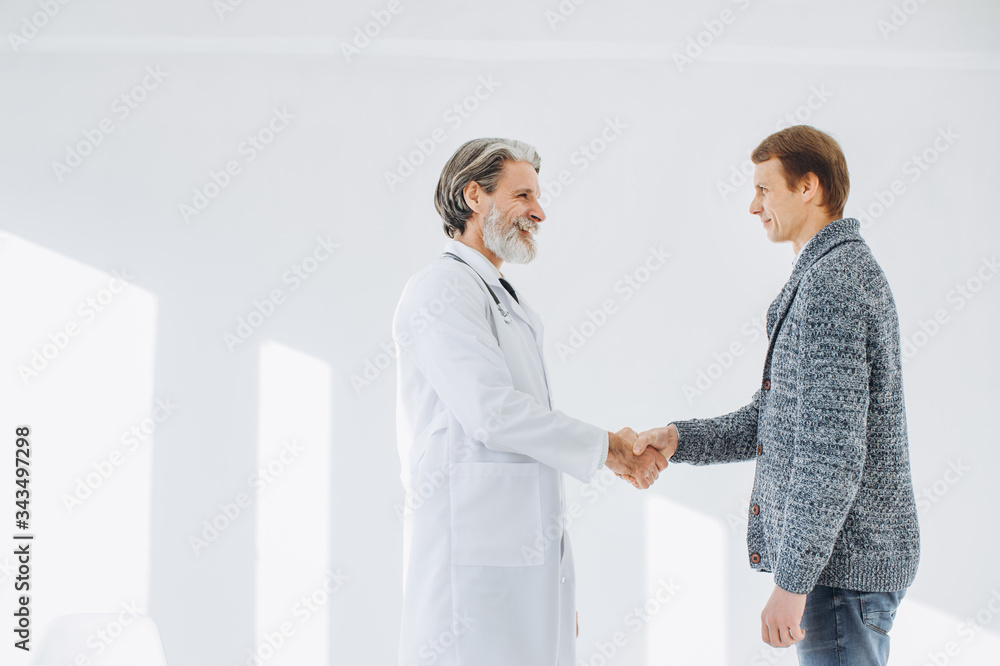 Senior doctor shaking hands with patient while meeting at doctor's office.